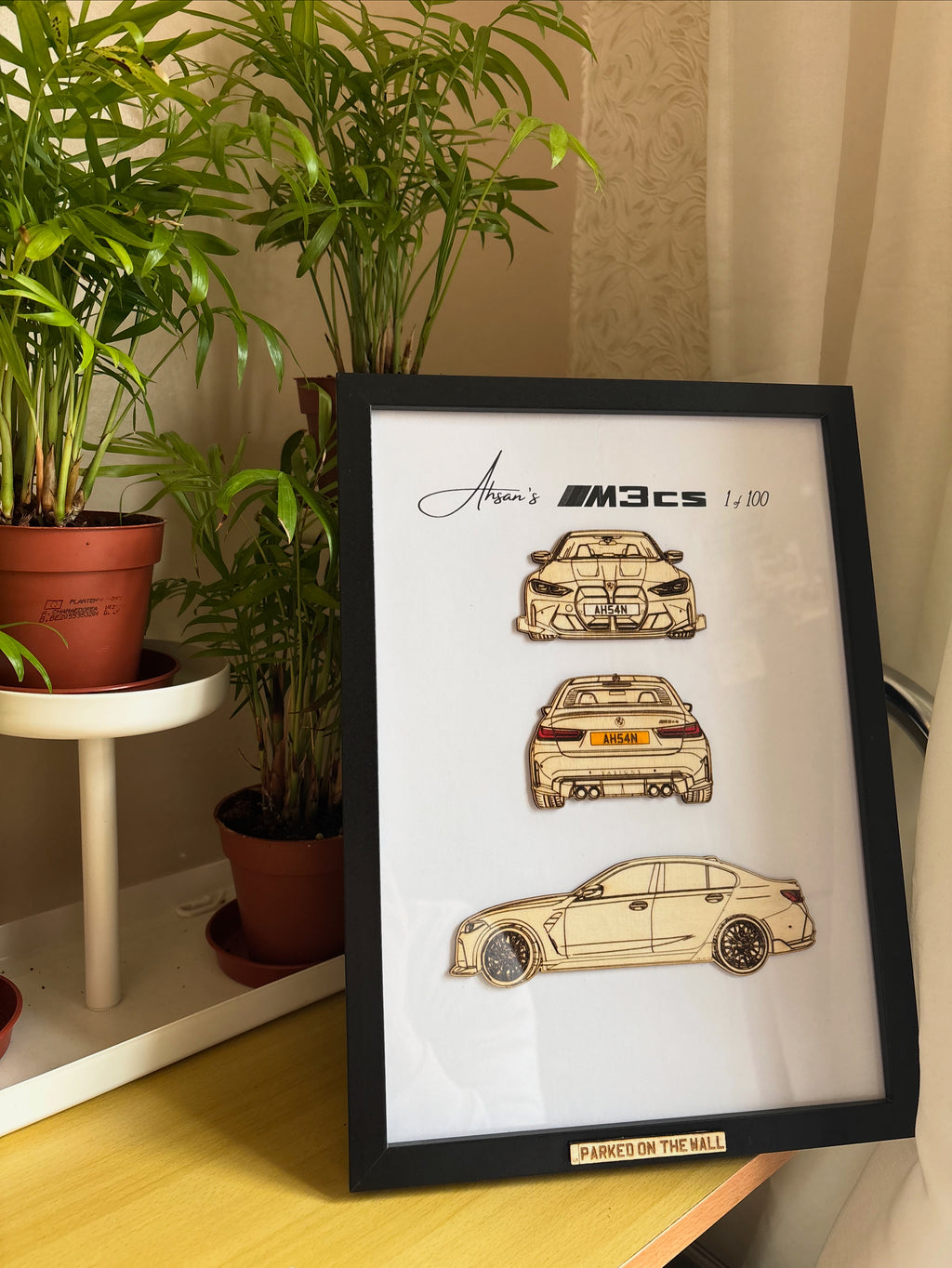Framed artwork of a car design on a table with plants in the background
